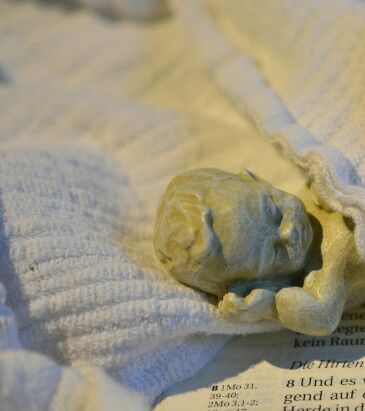 kleine Figur Kind gewickelt, liegt auf einer aufgeschlagenen Bibelseite. Foto: pixabay.com, pfarrbriefservice.de