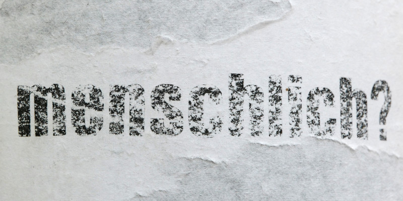 eine zerknitterte Ansicht des Wortes "menschlich", versehen mit einem Fragezeichen